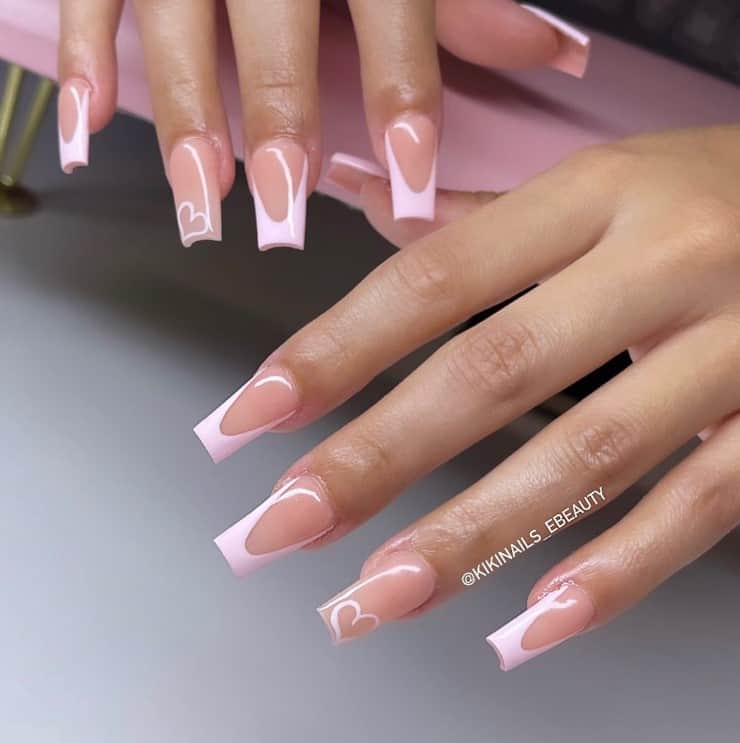 A woman's hands with nude peach nail polish base that has light pink French-tip nails and a big light pink heart at the upper left corner 