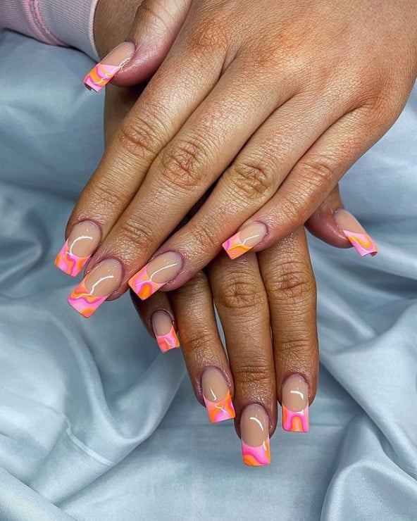 A closeup of a woman's hands with nude nail polish base that has a mix of bright orange with different shades of pink
