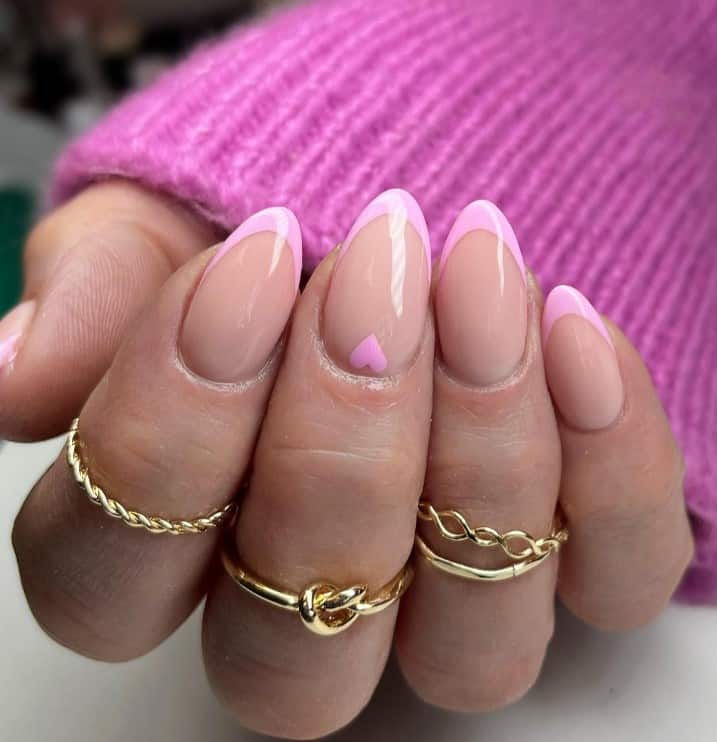 A closeup of a woman's hand with nude nail polish base that has thinly lined pink French tips and a pretty pink heart