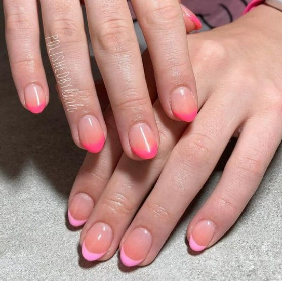 A closeup of a woman's hands with sheer peach ombré nail polish base that has hot pink tips on one hand and light pink tips on the other
