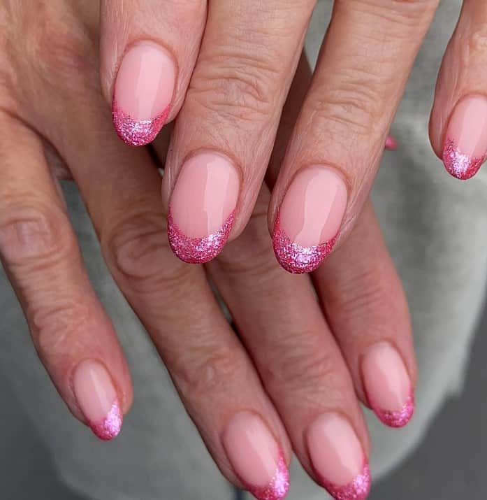 A closeup of a woman's hands with glossy baby pink nail polish base that has glitter French-tip nails in hot pink