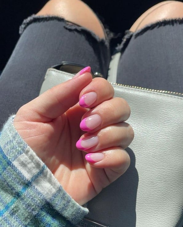 A woman's hand with nude nail polish base that has neon pink nail tips 