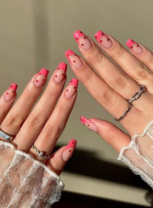 A woman's hands with nude nail polish base that has dark pink French tips and tiny orange studs