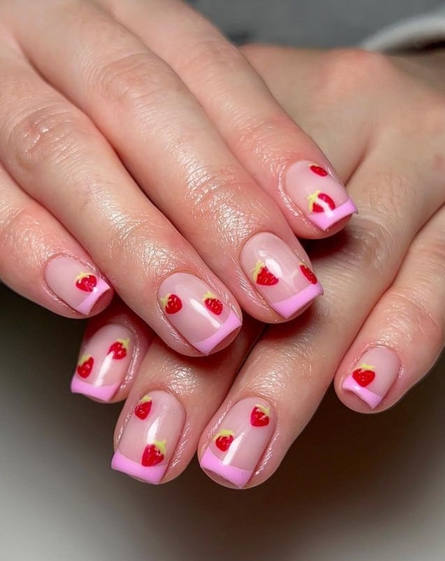 A closeup of a woman's hands with nude nail polish base that has pink tips and strawberry art