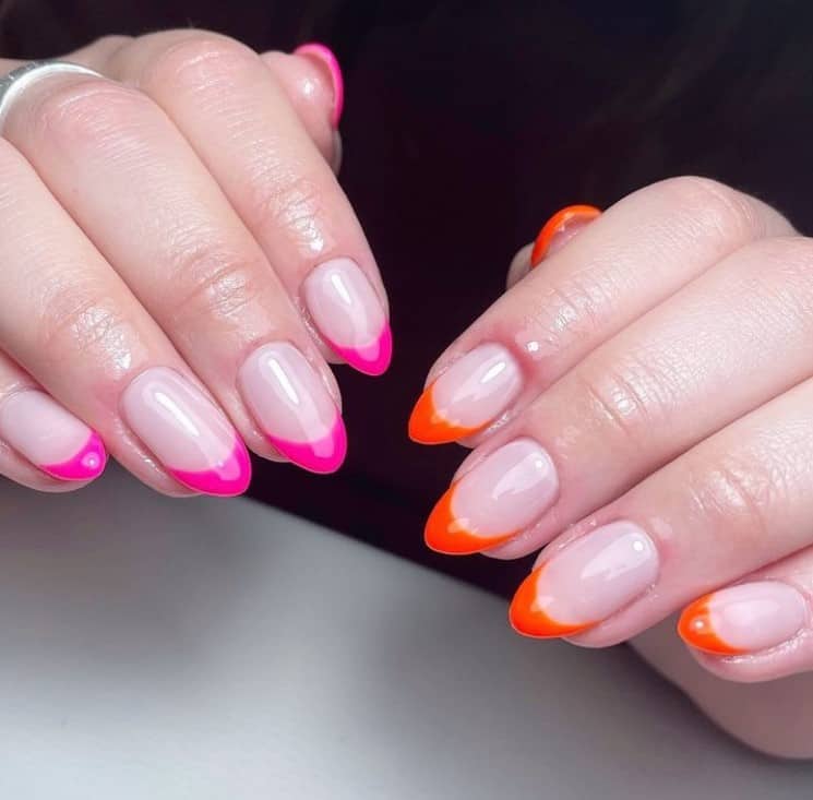 A closeup of a woman's hands with glossy nude nail polish that has vibrant orange French tips on one hand and bright pink tips on the other
