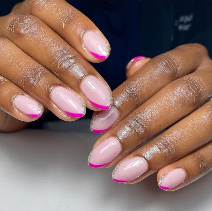 A closeup of a woman's hands with soft pastel pink nail polish base that has glittery silver and dark pink V-shaped French tips