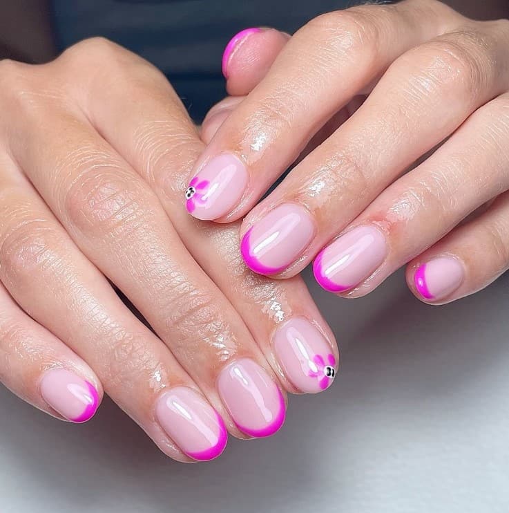 A closeup of a woman's hands with glossy nude pink nail polish that has fuchsia pink French tips and flower