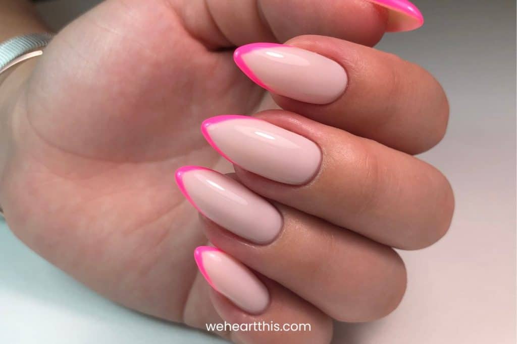A closeup of a woman's hand with nude nail polish base that has neon pink french tips