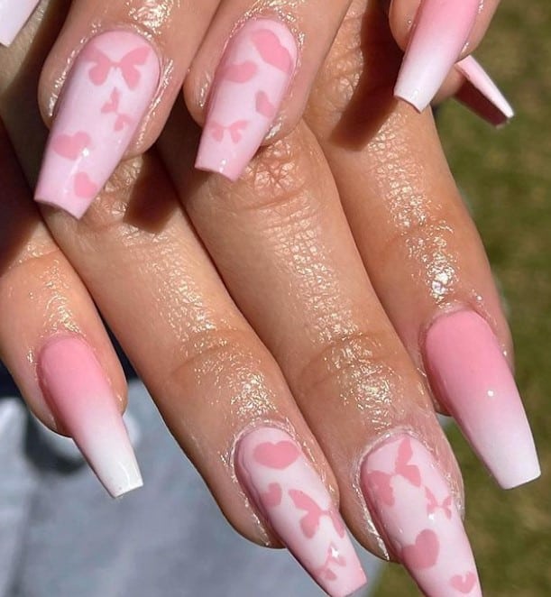 A closeup of a woman's fingernails with white and pink nail polish that has pink butterflies and heart silhouettes