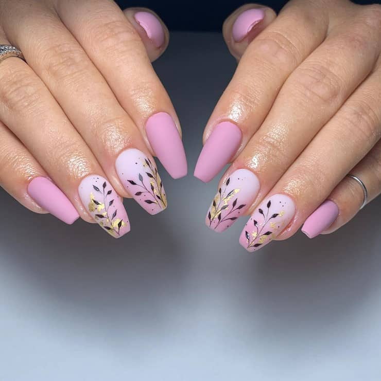 A closeup of a woman's fingernails with matte rose pink ombre accent nail polish that has leaf stem silhouettes and stunning smears of gold foil nail designs