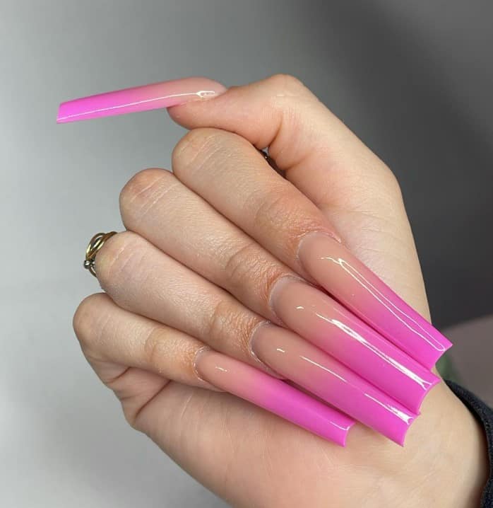 A closeup of a woman's long square acrylic fingernails with  ombre of pink and nude nail polish 