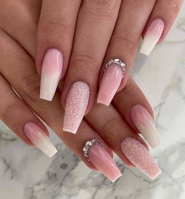 A closeup of a woman's fingernails with white and pink ombre nail polish that has sugary white glitter and jewels