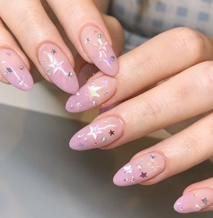 A closeup of a woman's fingernails with dusty pink-to-nude ombre nail polish that has rhinestones and clear stars designs