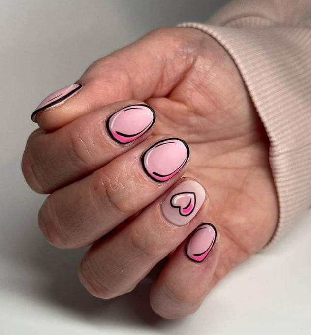 A closeup of a woman's fingernails with pastel pink nail polish that has heart cartoon nail designs