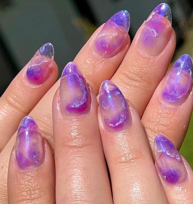 A closeup of a woman's hands with purple and white swirls that has almond-shaped jelly nails