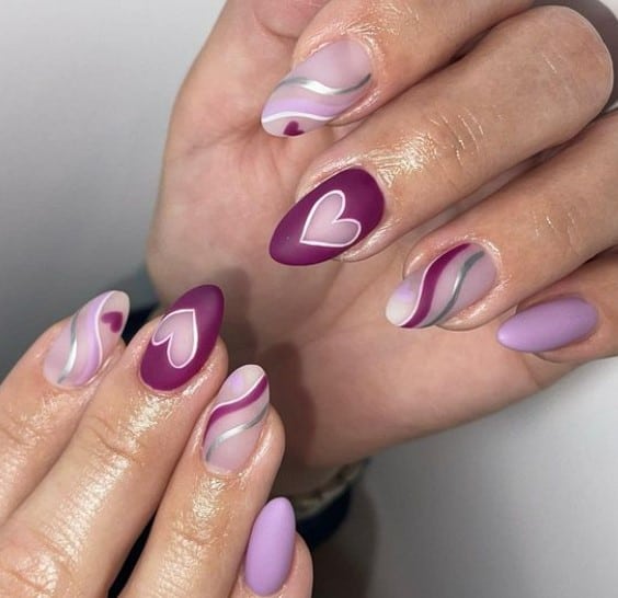 A closeup of a woman's fingernails with different shades of purple nail polish that has clean silver outlines and beautiful hearts nail designs