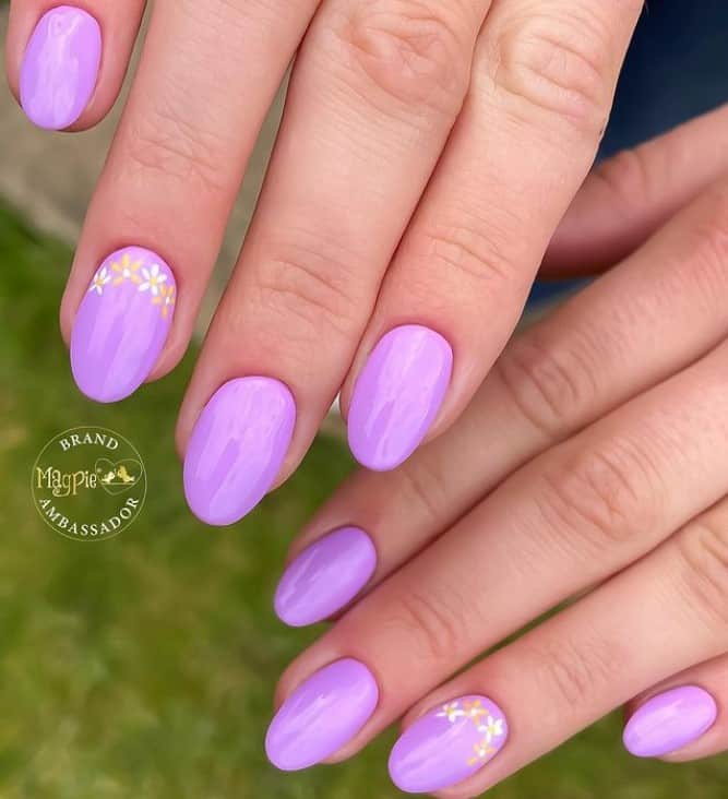 A closeup of a woman's fingernails with a glossy purple nail polish that has flowers nail designs