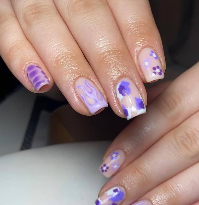 A closeup of a woman's fingernails with nude nail polish base that has flames, flowers, crocodile print, and paint splotches nail designs
