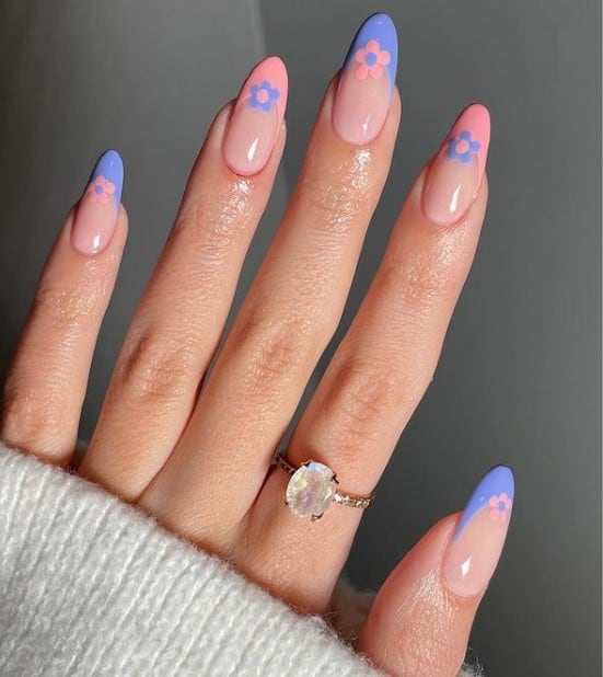 A closeup of a woman's fingernails with nude nail polish that has tiny flowers nail designs and salmon and periwinkle nail tips 