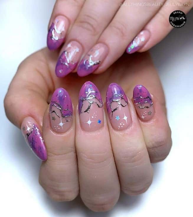 A closeup of a woman's fingernails with nude nail polish that has star stickers and intricate silver chrome swirls and purple tips