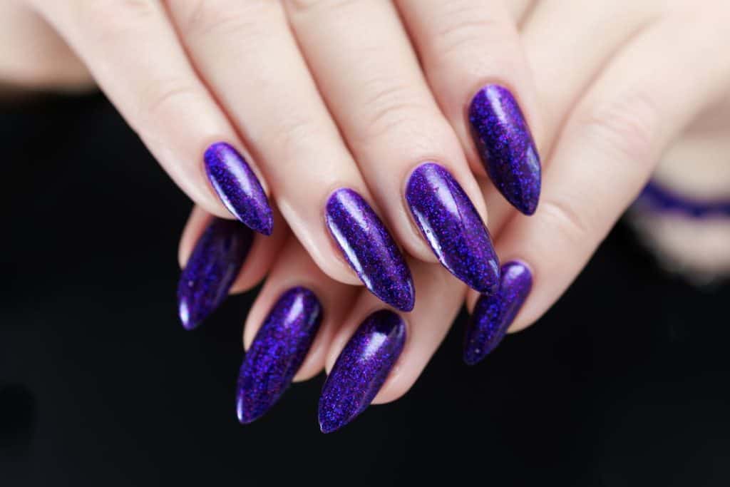 A closeup of a woman's fingernails with dark purple nail polish that has glitter 