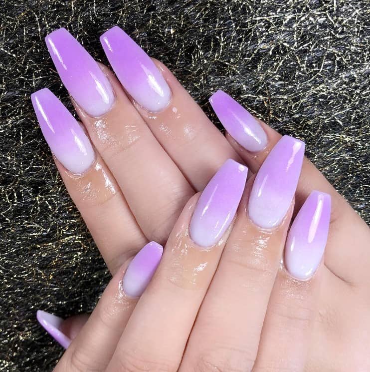 A closeup of a woman's fingernails with purple nail polish that has a soft gradient effect