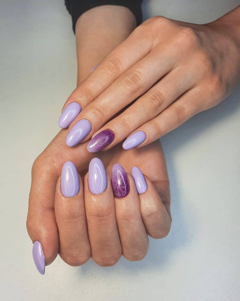 A woman's beautiful fingernails with a light  and dark purple nail polish that has white glitter 