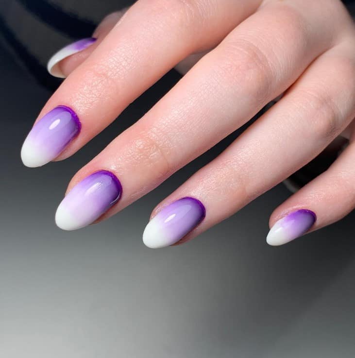 A closeup of a woman's fingernails with a glossy milky white base and a deep and rich shade of purple at the cuticles