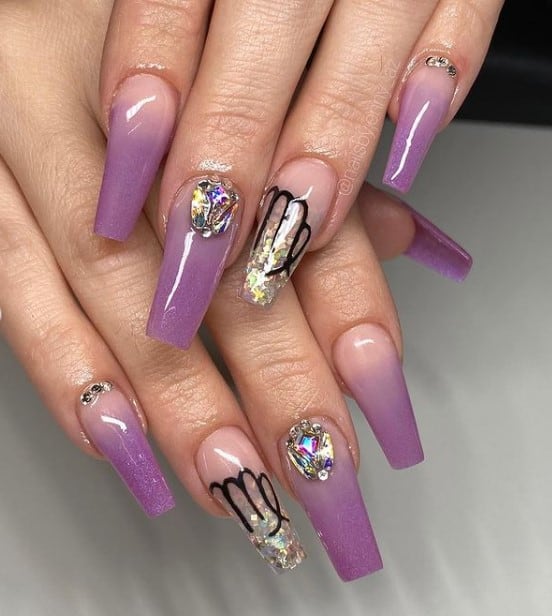 A closeup of a woman's fingernails with nude to purple nail polish that has Virgo symbol, glitter and rhinestones as nail designs