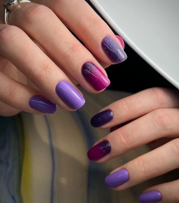 A closeup of a woman's beautiful fingernails with different shades of purple ombré nail polish that has glitter nail designs