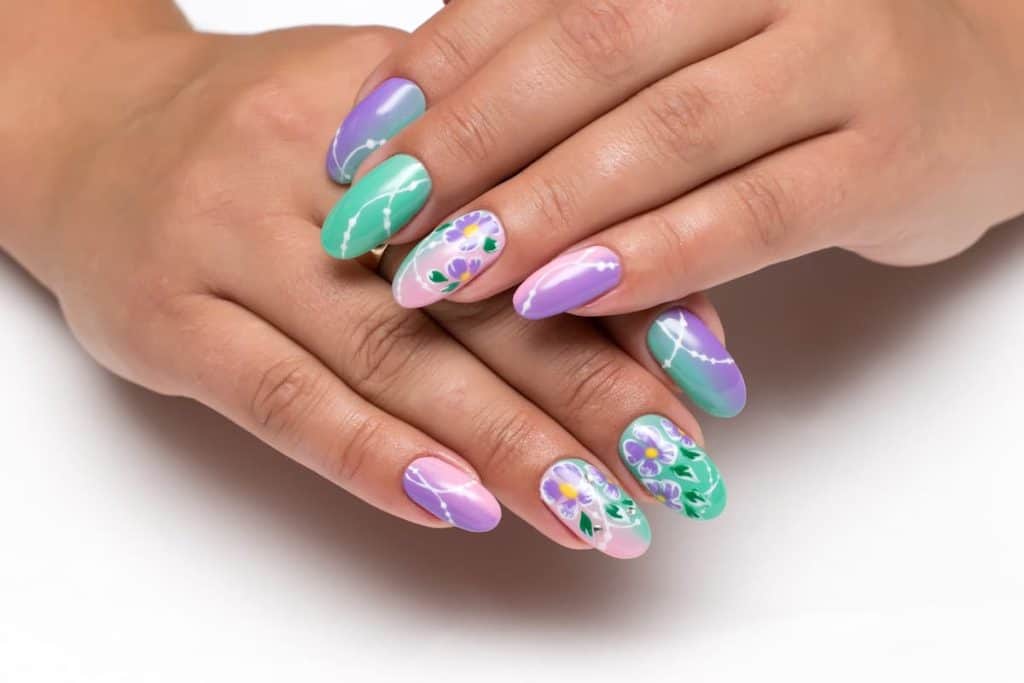 A closeup of a woman's beautiful fingernails with gorgeous ombré of purple, pink, green nail polish that has purple floral nail art on accent nails