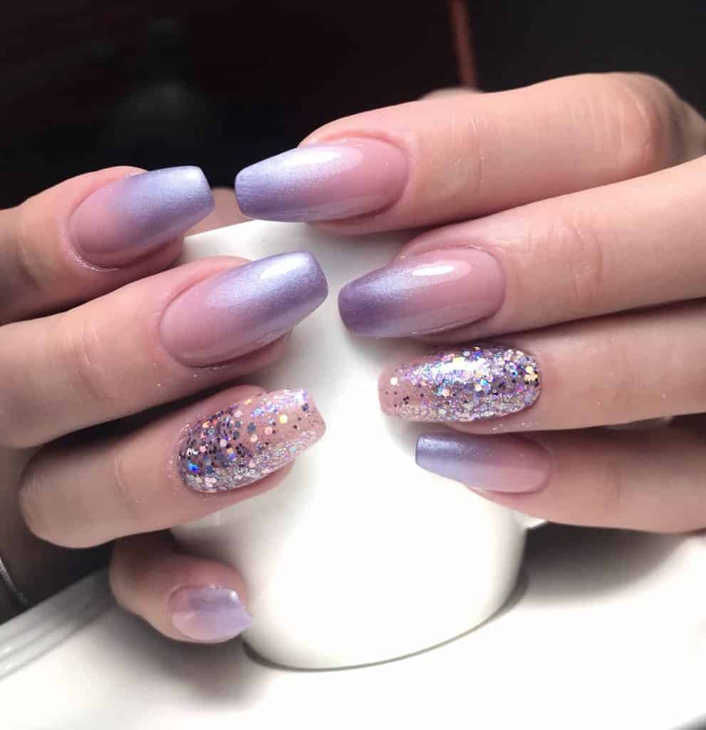 A closeup of a woman's fingernails with metallic gradient of lavender nail polish that has chunky holographic glitter on select nails