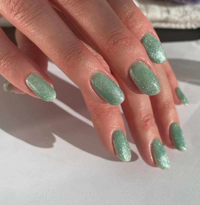 A closeup of a woman's fingernails with light sage green nail polish that has glitter