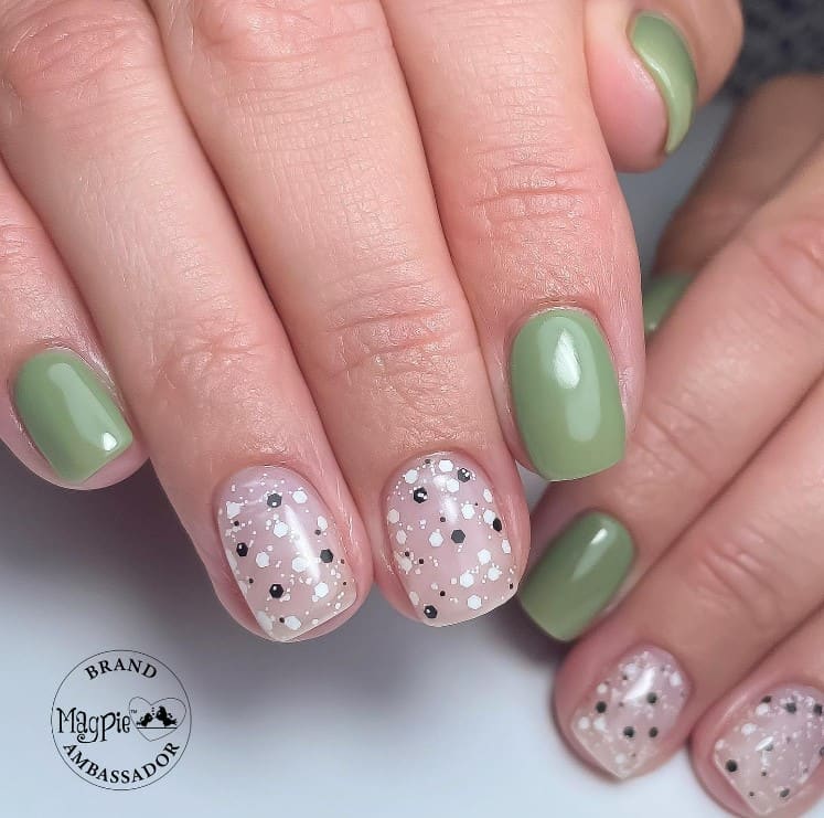 A closeup of a woman's fingernails with a nude and sage green nail polish that has black and white splatter-like dots on nude nails
