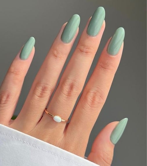A closeup of a woman's long fingernails with a glossy sage green nail polish 