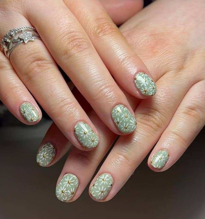 A closeup of a woman's fingernails with a sage green nail polish that has floral nail designs