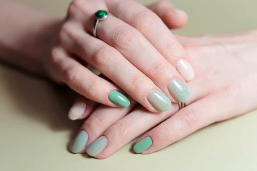 A woman's fingernails with a different shades of sage green ombré nail polish that has gold flecks on select nails