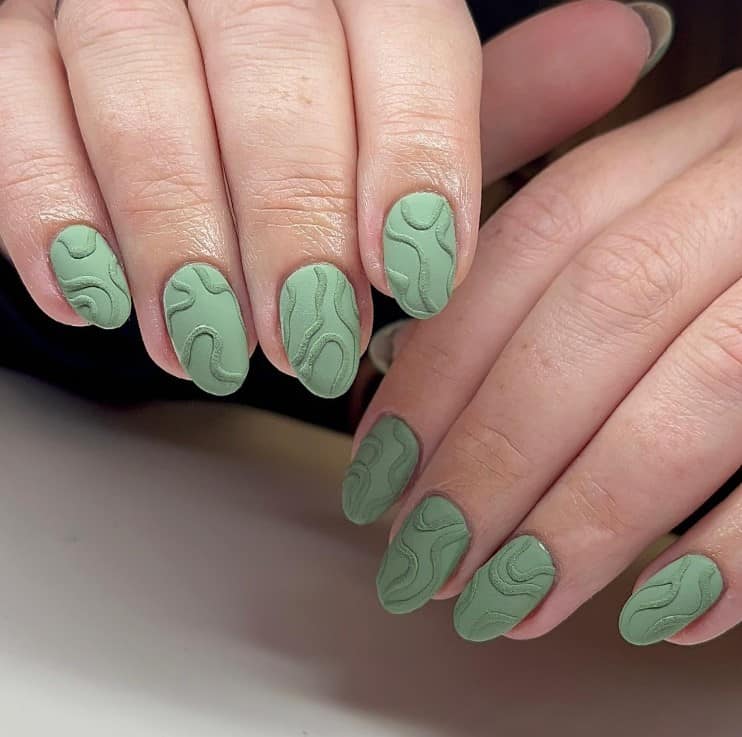 A closeup of a woman's fingernails with a matte sage green nail polish that has 3D swirls 