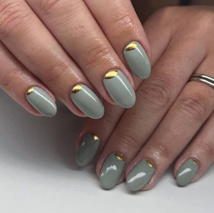 A closeup of a woman's fingernails with a dark sage green nail polish that has an inverted French tip using chrome gold polish