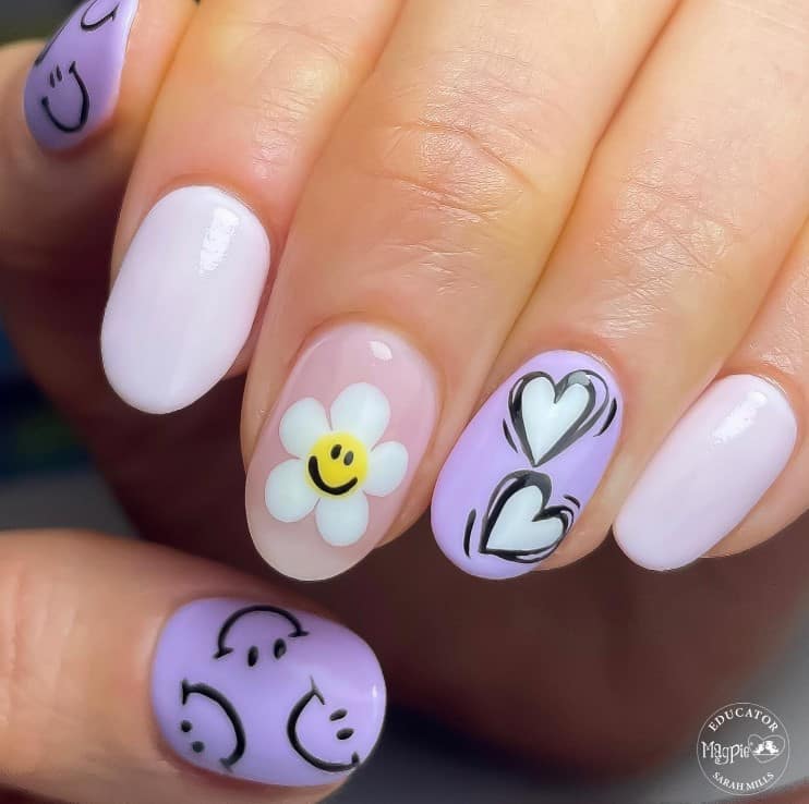 A closeup of a woman's fingernails with combination of lavender, white, and baby pink nail polish that has hearts, daisies, and smileys nail designs