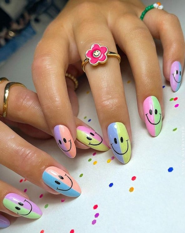 A closeup of a woman's fingernails with complementing pastel colors in halves  nail polish that has a smiley face in black nail designs