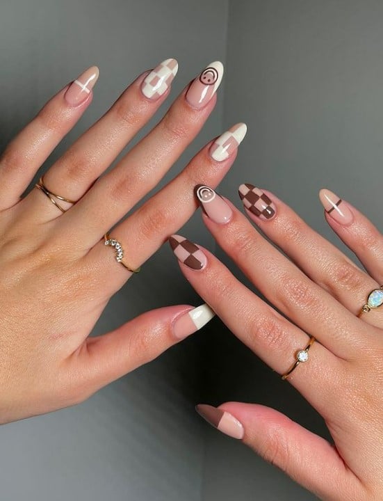 A woman's fingernails with a different shades of brown nail polish that has smileys, lines, French tips, and checkerboards nail designs