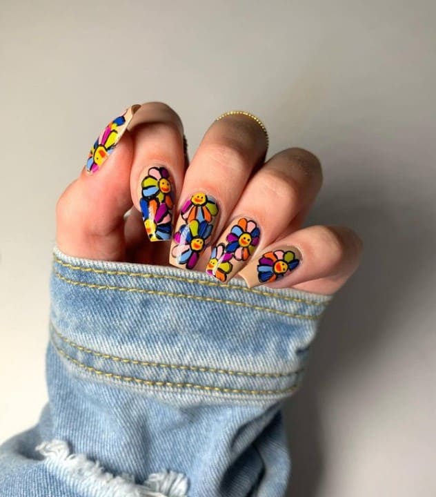 A woman's fingernails with a nude nail polish that has Takashi Murakami’s iconic flower smiley with thick black outlines nail designs