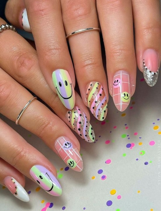 A closeup of a woman's fingernails with multicolored pastel nail polish that has  pastel smiley faces, stripes, dots, glitter French tip, glitter swipes, and grid lines