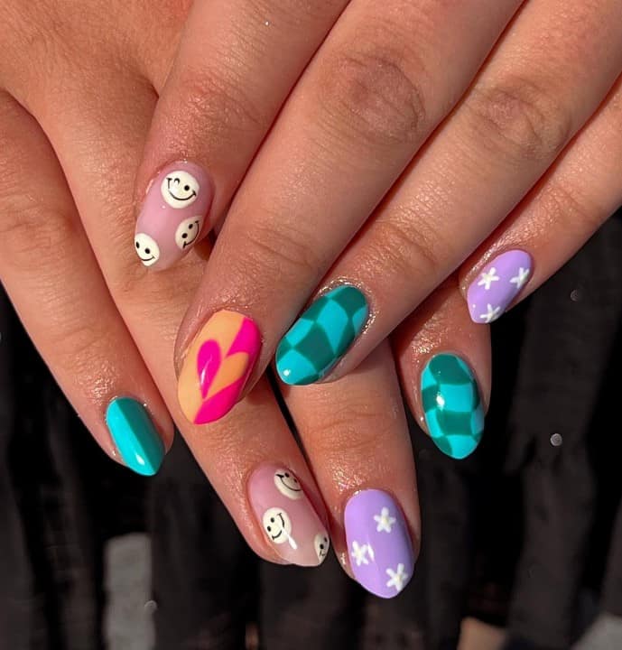 A closeup of a woman's fingernails with retro color combinations nail polish that has checkers, flowers, and a heart nail designs