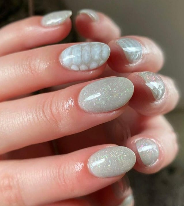 A closeup of a woman's hands with white nail polish base that has a snakeskin print and a glittery finish