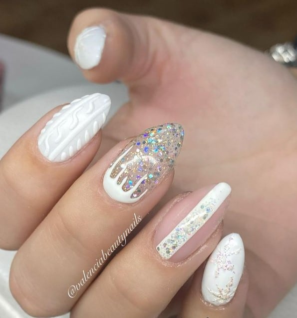 A closeup of a woman's hand with white and nude nail polish base that has snowflakes, melted snow, chunky glitter, and knitted-sweater patterns