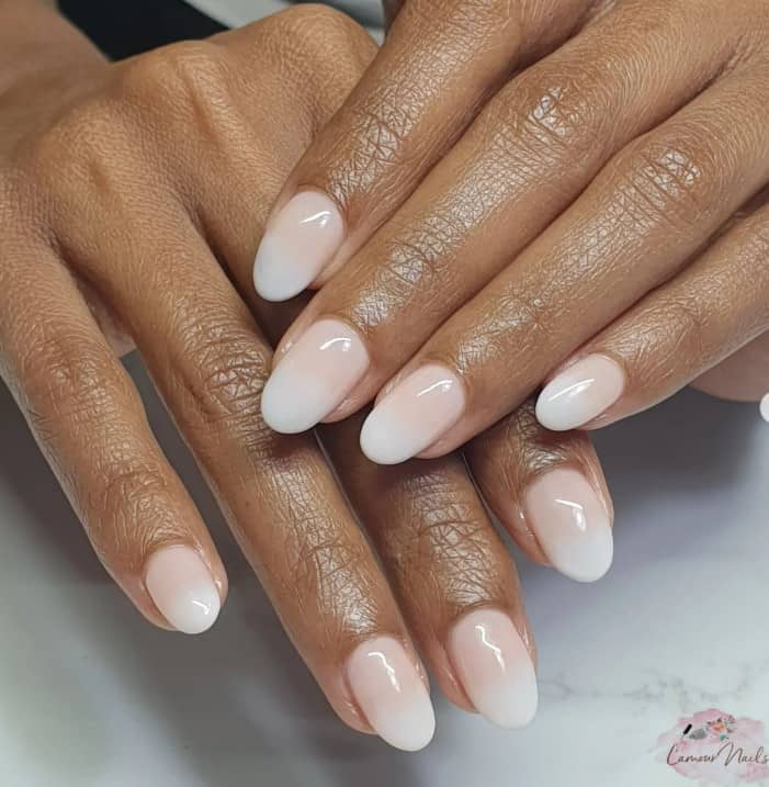 A closeup of a woman's medium-length oval fingernails with ombré nails in nude and white