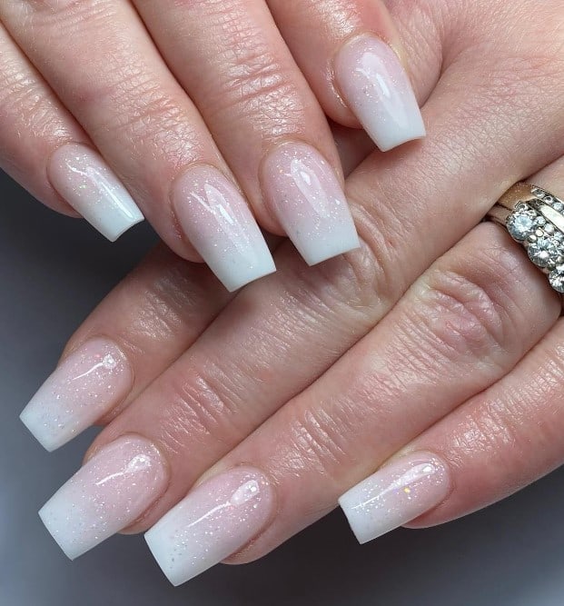 A closeup of a woman's fingernails with beige ombré nails that has glittery top coat over the nude-and-white