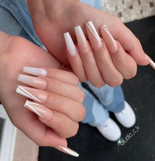 A woman's fingernails with beige ombré acrylic nails that has white diagonal tips